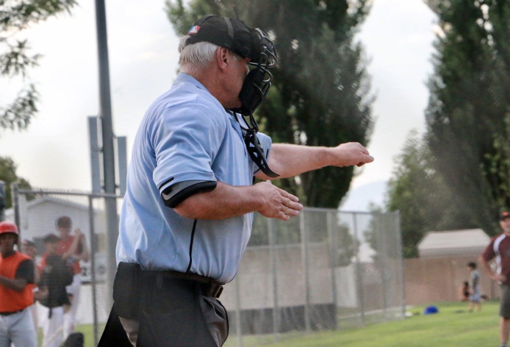 Baseball umpire in blue uniform making signal for third strike, you’re out, hand signals.